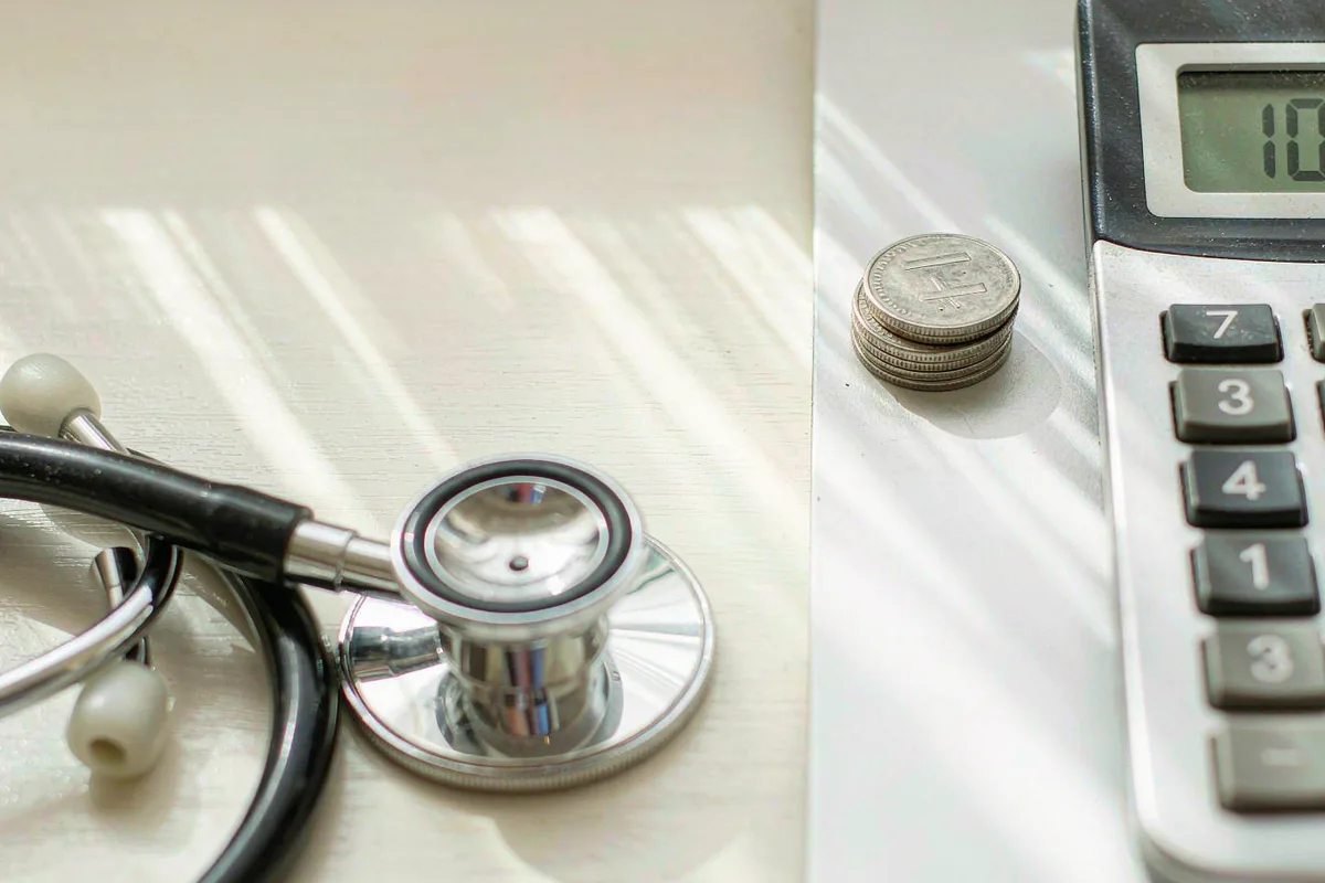 Stethoscope resting beside a stack of coins and a calculator