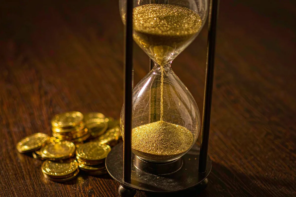 Glass hourglass beside a pile of gold coins