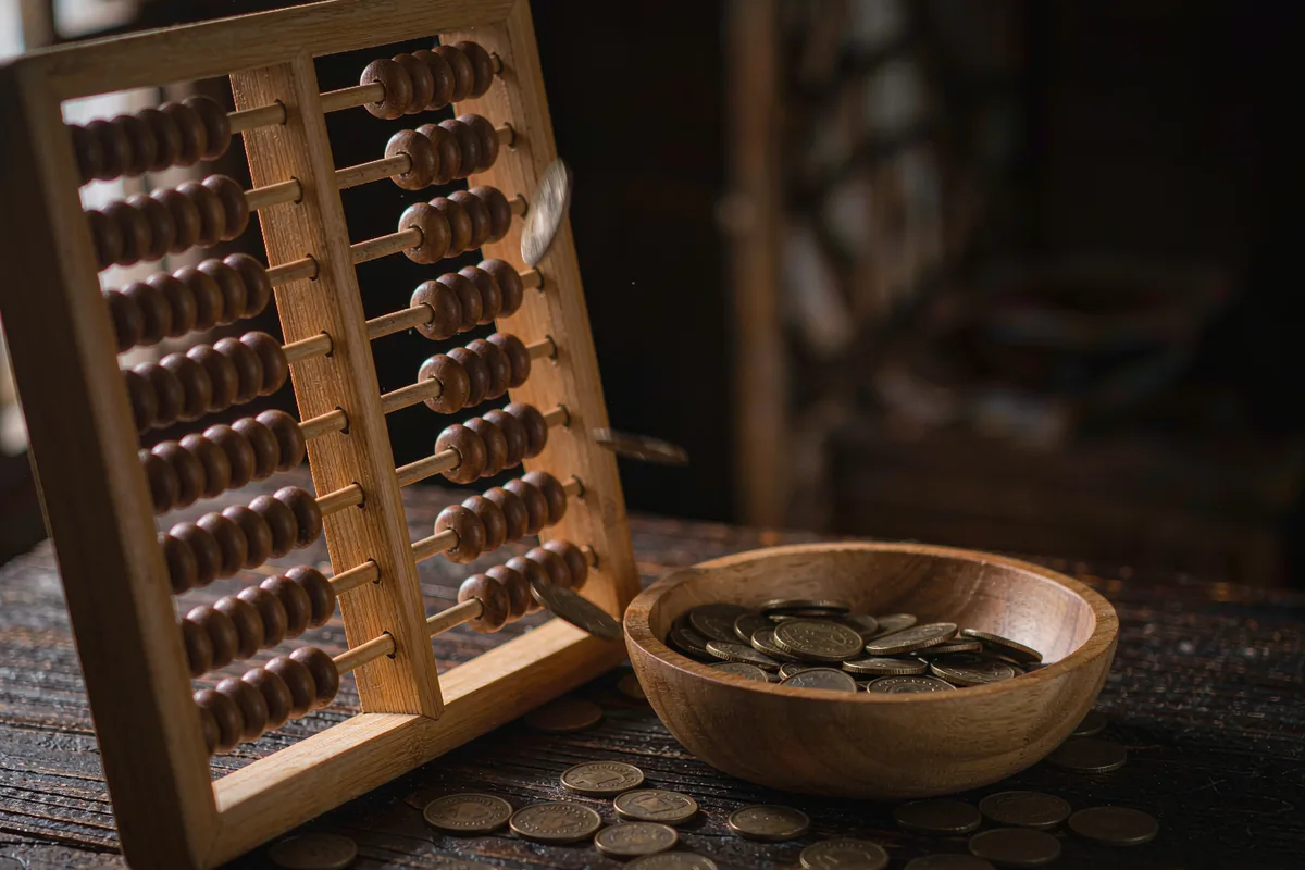 Wooden abacus with beads mid-slide beside coins