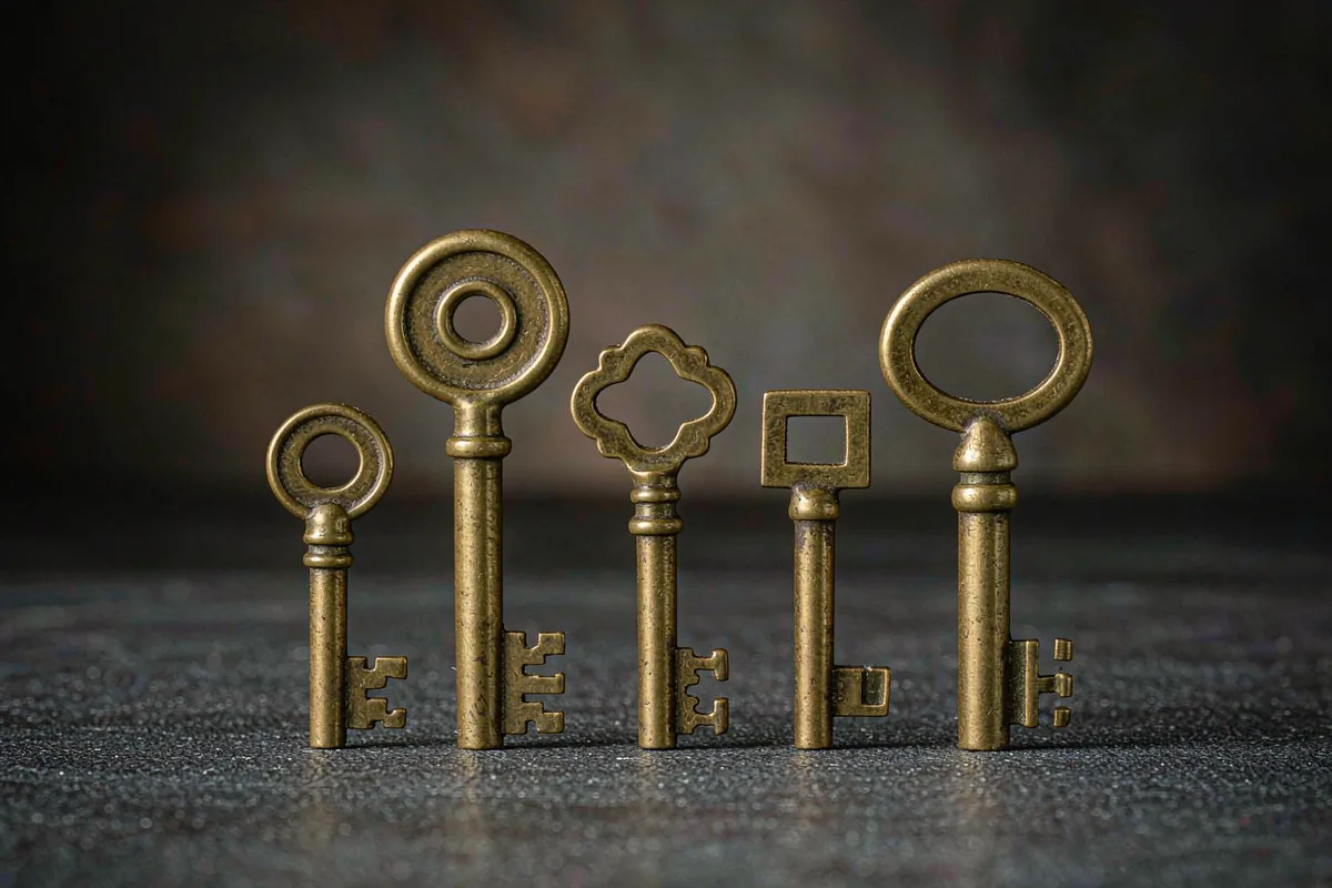Five antique brass keys in a row on dark slate