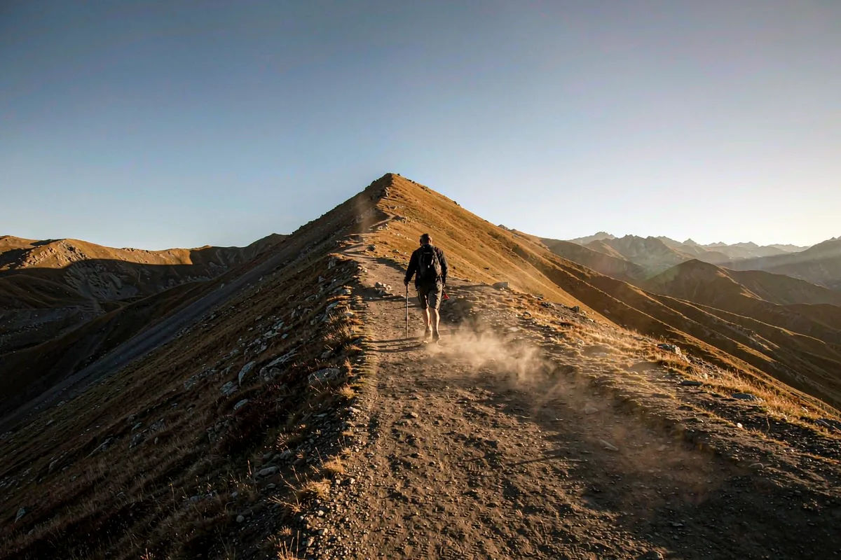 Hiker walking a mountain trail toward a sunlit summit