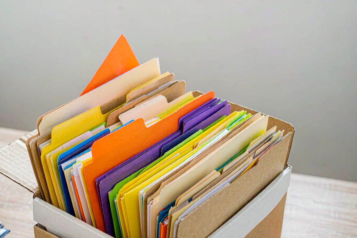 Open cardboard box filled with colorful paper folders on a desk