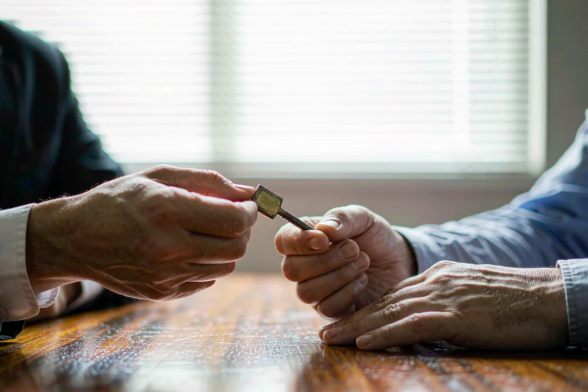 One hand passing a brass key to another across a desk